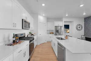 Kitchen featuring appliances with stainless steel finishes, light hardwood / wood-style floors, a kitchen island with sink, and white cabinets