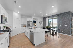 Kitchen with sink, light hardwood / wood-style flooring, appliances with stainless steel finishes, a kitchen island with sink, and white cabinetry