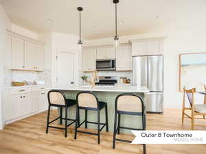 Kitchen featuring white cabinetry, a kitchen island with sink, stainless steel appliances, a kitchen bar, and decorative light fixtures