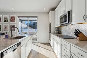 Kitchen featuring white cabinetry, sink, light hardwood / wood-style floors, stainless steel appliances, and light stone countertops