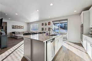 Kitchen with appliances with stainless steel finishes, white cabinetry, sink, a kitchen island with sink, and light hardwood / wood-style flooring