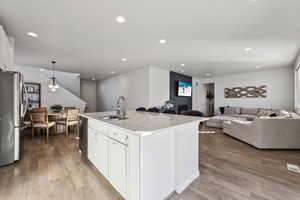 Kitchen featuring decorative light fixtures, sink, white cabinets, stainless steel appliances, and a center island with sink