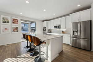 Kitchen featuring dark wood-type flooring, appliances with stainless steel finishes, a kitchen island with sink, white cabinetry, and decorative backsplash