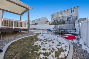 Yard covered in snow with a deck and a trampoline