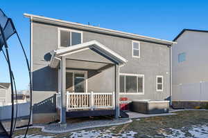 Snow covered back of property with a wooden deck and a hot tub