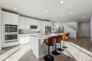 Kitchen featuring stainless steel appliances, white cabinetry, hanging light fixtures, and a kitchen island with sink