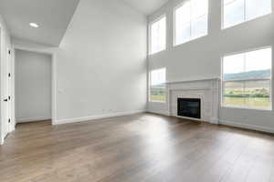 Unfurnished living room featuring a tiled fireplace, light wood finished floors, a towering ceiling, a mountain view, and recessed lighting