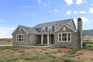 View of front facade featuring covered porch, stone siding, a shingled roof, and a chimney