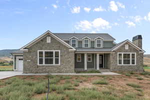 View of front facade featuring a porch, stone siding, a chimney, and a shingled roof