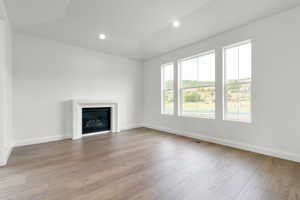 Unfurnished living room with recessed lighting, a glass covered fireplace, light wood-style floors, and lofted ceiling