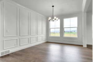 Unfurnished dining area featuring a decorative wall, a chandelier, wood-type flooring, and ornamental molding