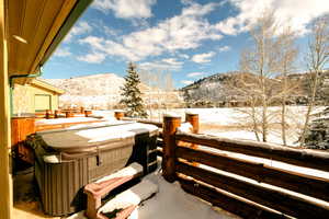 Snow covered patio with a hot tub and a mountain view