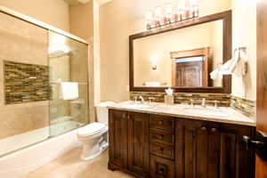 Full bathroom featuring combined bath / shower with glass door, backsplash, tile patterned flooring, vanity, and toilet