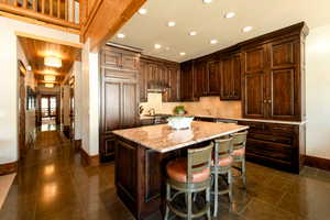 Kitchen featuring a breakfast bar, tasteful backsplash, a center island, dark brown cabinetry, and light stone countertops