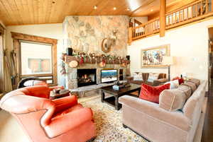 Living room featuring wood ceiling, lofted ceiling, and a stone fireplace