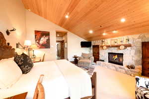 Bedroom featuring vaulted ceiling, a stone fireplace, and wood ceiling