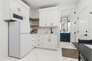 Kitchen with white cabinetry, white appliances, light tile patterned flooring, and sink