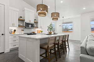 Kitchen featuring a kitchen island with sink, hanging light fixtures, backsplash, a wealth of natural light, and white cabinets