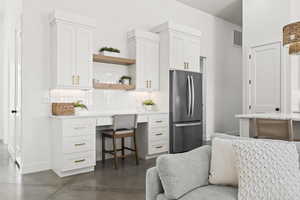 Kitchen with stainless steel refrigerator, white cabinetry, built in desk, and tasteful backsplash