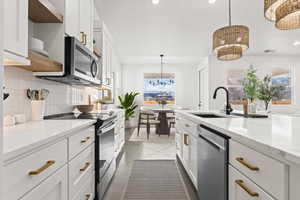 Kitchen featuring pendant lighting, sink, white cabinetry, backsplash, and stainless steel appliances