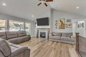 Living room with a tile fireplace, high vaulted ceiling, ceiling fan, and light hardwood / wood-style floors