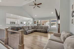 Living room featuring sink, ceiling fan with notable chandelier, light hardwood / wood-style floors, and high vaulted ceiling