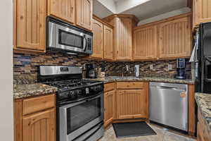 Kitchen with sink, backsplash, dark stone counters, and appliances with stainless steel finishes