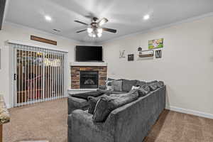 Living room featuring ceiling fan, ornamental molding, a fireplace, and carpet floors