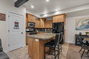 Kitchen with range with gas stovetop, a breakfast bar area, backsplash, a center island, and light stone counters