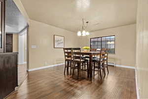 Dining area featuring a baseboard heating unit, dark wood-type flooring, a notable chandelier, and a textured ceiling