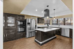 Kitchen featuring island exhaust hood, a kitchen island, dark brown cabinetry, and black appliances