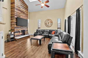 Living room with ceiling fan, baseboard heating, hardwood / wood-style floors, high vaulted ceiling, and a multi sided fireplace