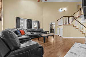 Living room featuring beam ceiling, hardwood / wood-style flooring, ceiling fan, and a high ceiling