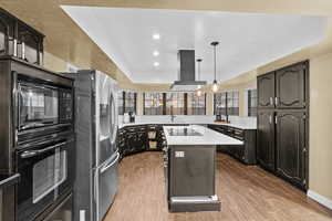 Kitchen with pendant lighting, sink, a center island, black appliances, and island exhaust hood