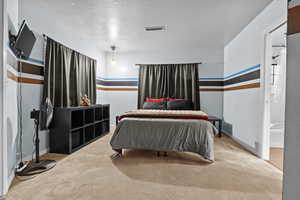 Carpeted bedroom featuring ensuite bath and a textured ceiling