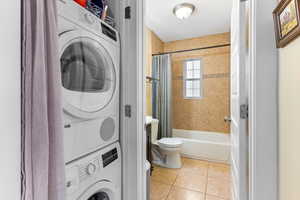 Washroom featuring stacked washer / drying machine and light tile patterned floors