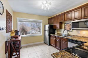 Kitchen featuring dark stone countertops, sink, light tile patterned floors, and stainless steel appliances