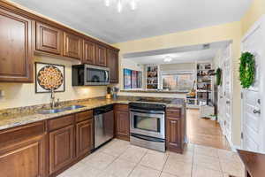 Kitchen with light stone counters, stainless steel appliances, kitchen peninsula, and sink