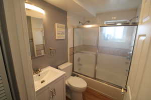 Full bathroom featuring enclosed tub / shower combo, vanity, toilet, and wood-type flooring