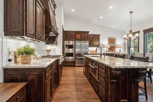 Kitchen with sink, a breakfast bar area, a large island with sink, stainless steel appliances, and light stone countertops