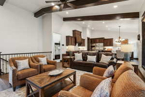 Living room featuring ceiling fan with notable chandelier, light hardwood / wood-style flooring, and lofted ceiling with beams