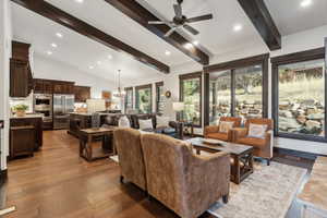 Living room with ceiling fan with notable chandelier, wood-type flooring, and lofted ceiling with beams