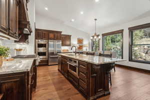 Kitchen with hanging light fixtures, a kitchen breakfast bar, an island with sink, and appliances with stainless steel finishes