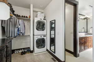 Laundry area featuring stacked washer / drying machine, light tile patterned floors, sink, and a chandelier