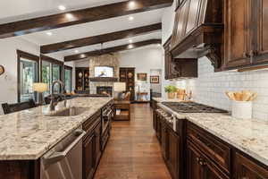 Kitchen with stainless steel appliances, sink, vaulted ceiling with beams, and light stone counters