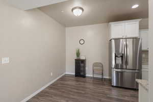 Kitchen featuring dark hardwood / wood-style floors, white cabinets, light stone counters, and stainless steel fridge with ice dispenser