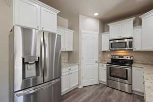 Kitchen featuring stainless steel appliances, wood-type flooring, light stone countertops, and white cabinets