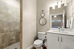 Bathroom featuring ceiling fan, tiled shower, vanity, and toilet