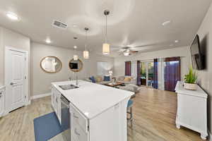 Kitchen featuring decorative light fixtures, sink, white cabinets, a kitchen island with sink, and light hardwood / wood-style floors