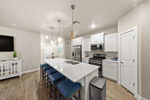 Kitchen with decorative light fixtures, white cabinetry, sink, stainless steel appliances, and a center island with sink